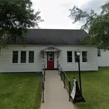 A simple, vinyl sided structure with concrete ramp to the red door